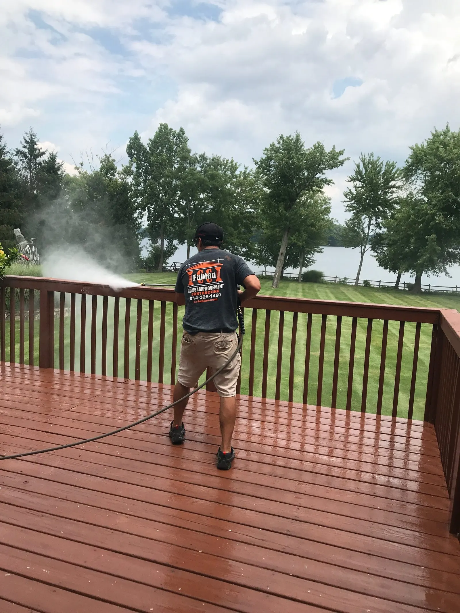 Worker power washing a stained deck, spray mist rising
