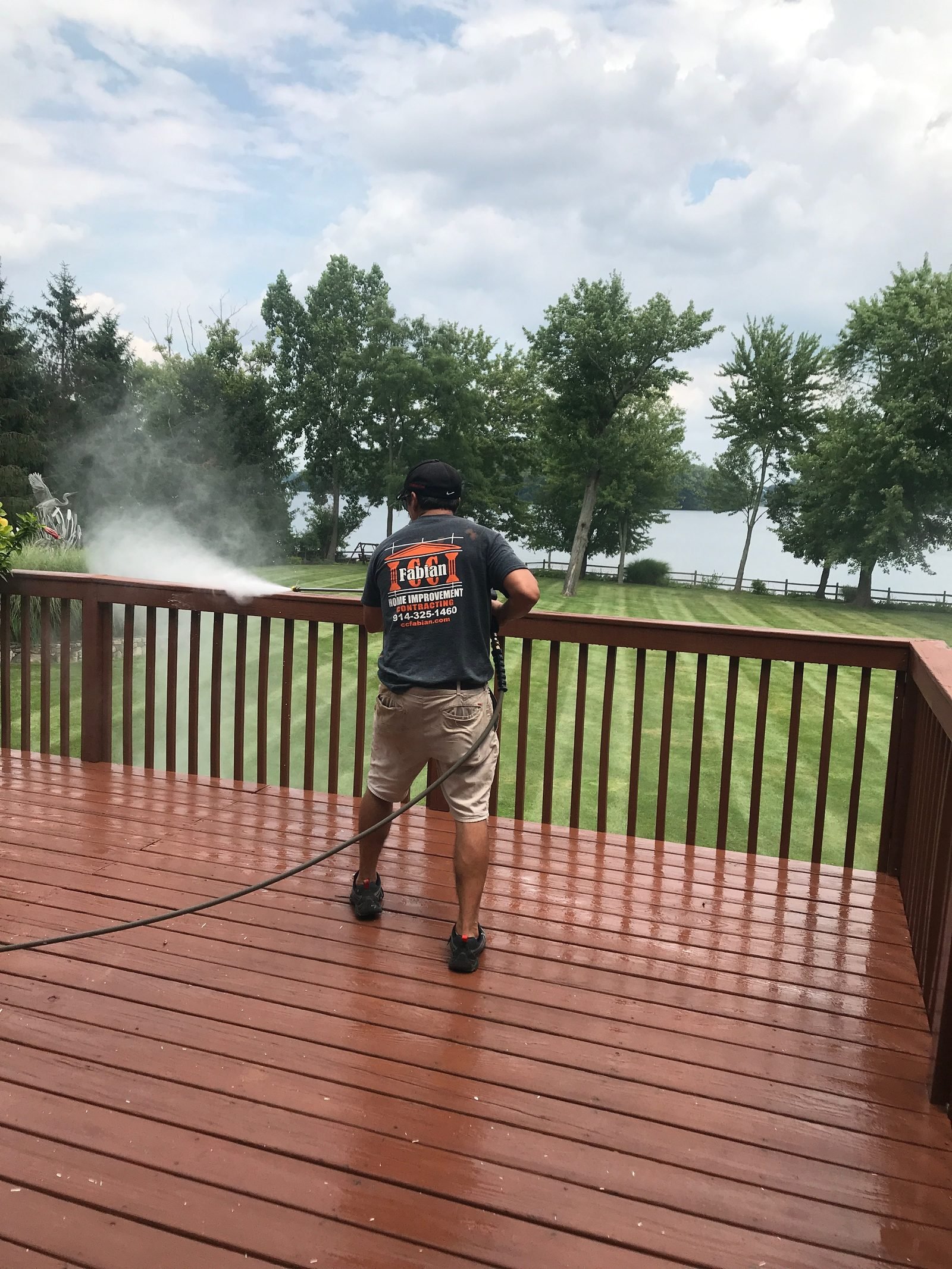 Worker power washing a stained deck, spray mist rising