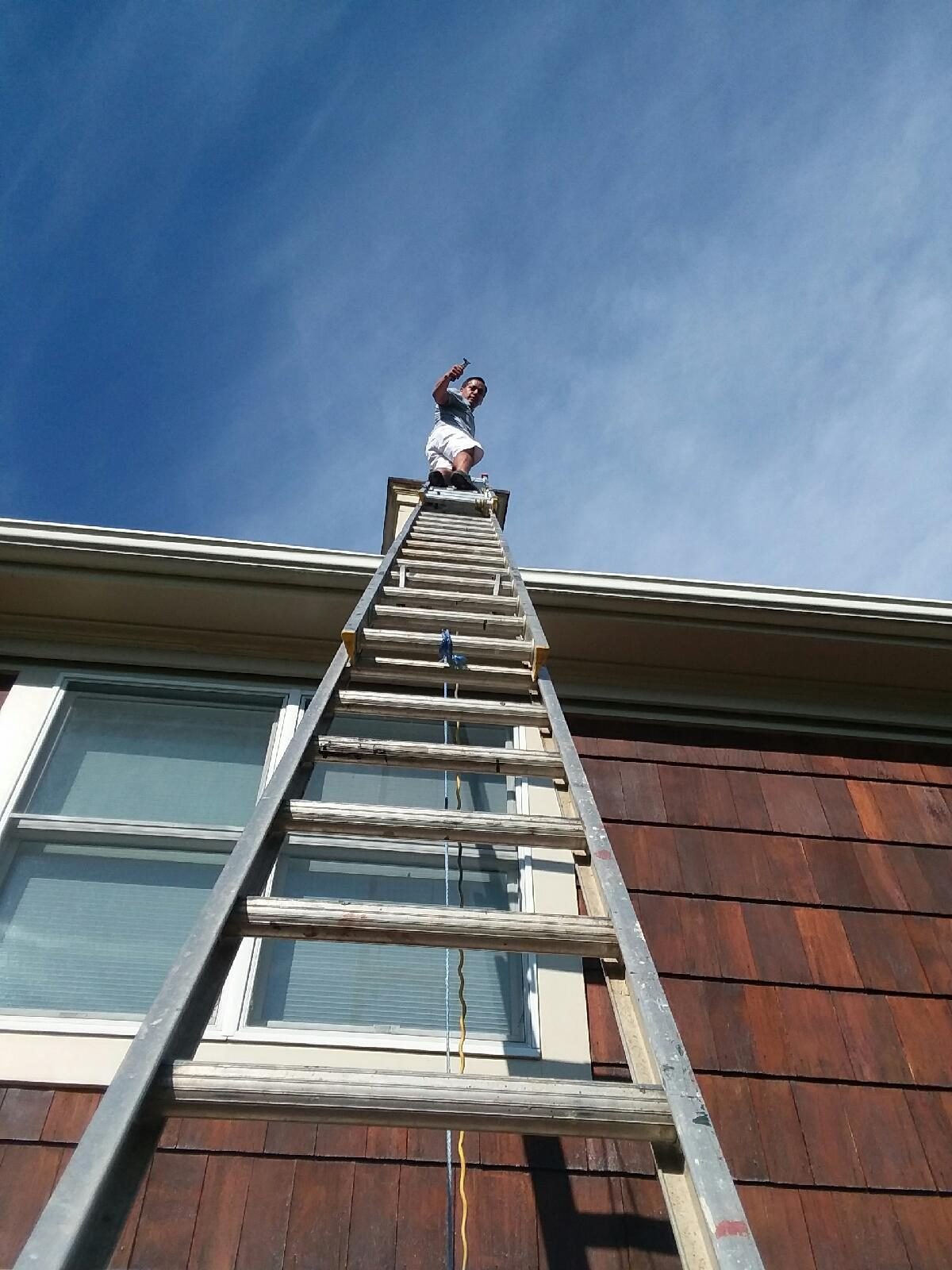 Crew member atop an extension ladder cleaning cedar shingle siding
