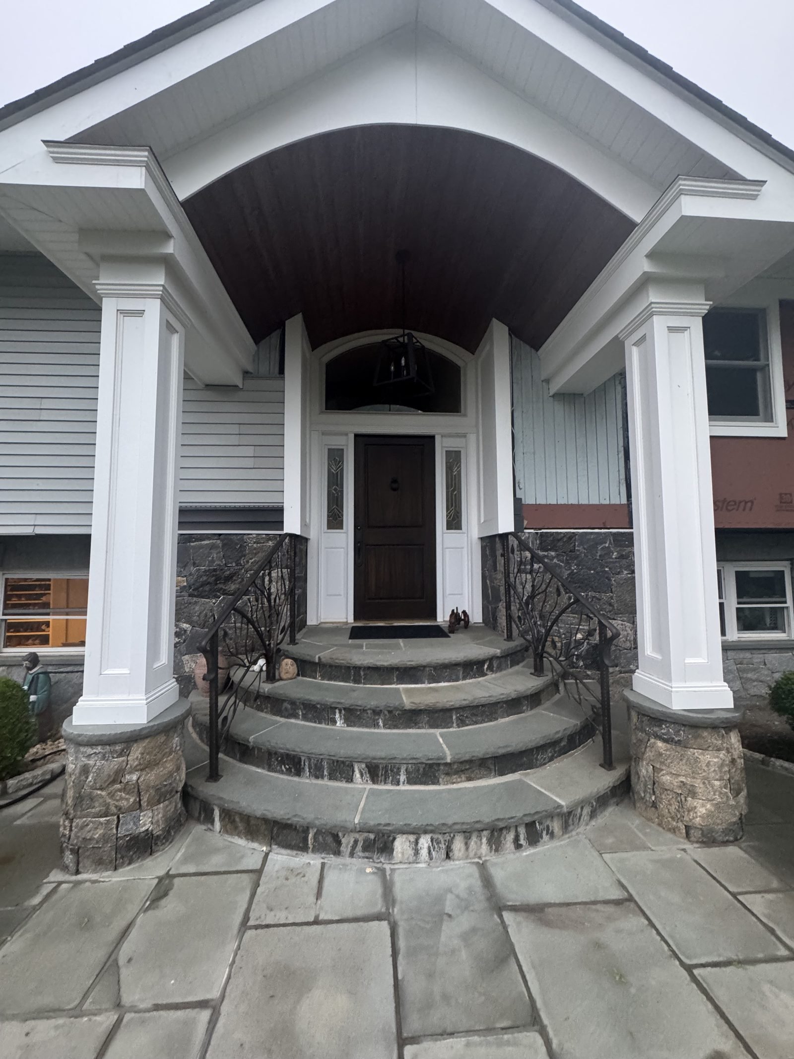 Completed home with a new columned portico, gray siding and stone entry steps
