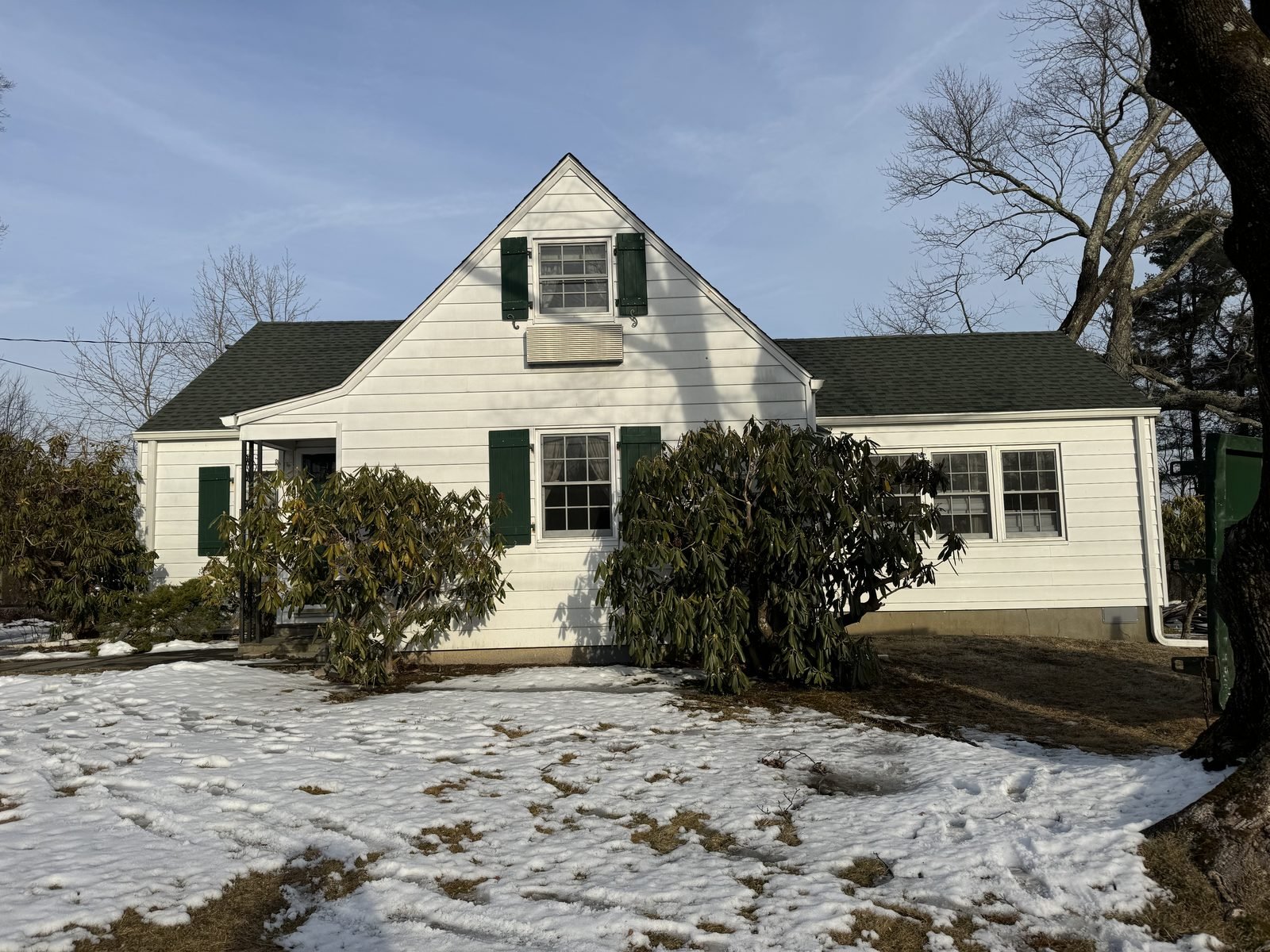 White cape home with green shutters before new siding